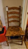 Front view of a wooden ladder back dining chair showing four curved horizontal slats and a solid seat with visible wood grain.