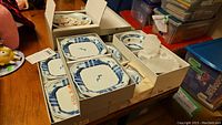Photo showing boxed sets of ceramic plates and bowls with blue traditional patterns, square shape, in original packaging.