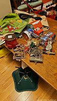 Wide view of Christmas-themed holiday décor items including tree stand, fabric ribbons, tins, and stocking holders on wooden table.