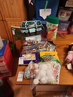 Craft supplies including colored pencils, ornaments, stickers, organizer bag, gift bag, and small planters all laid out on a table