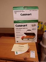 Original boxed packaging of the Cuisinart 4-Slice Belgian Waffle Iron model WAF-4BC with instruction booklet placed on top.