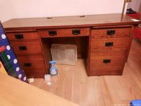 Front view of the wooden desk showing two doors and multiple drawers with black metal handles.