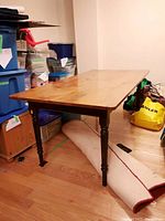View of rectangular wood dining table on hardwood floor, showing natural wood top and dark turned legs.