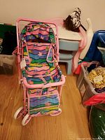 Full view of pink metal frame doll stroller with multicolor fabric seat and white wheels, showing condition and structure