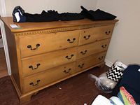 Front view of a light wood dresser with six drawers and black metal handles, showing some items on top not included in sale.