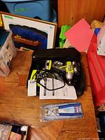 Ryobi cordless drill with battery attached, charger, black carrying case, papers, and glass cutter tool on wooden table