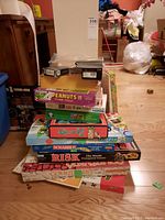Stack of boxed games and puzzles showing titles including Peanuts Sticker Puzzle, Risk The World Conquest Game, Scrabble, and others.