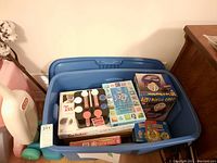Large blue bin filled with boxed games including Twister, Monte Carlo Poker Set, Bingo Cage, Rainbow Fish Memory Game, and more.