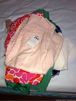 Stack of assorted ladies clothing including a pink sleeveless top, green and multicolor patterned items, and white short sleeve top.