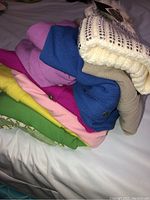 Stack of colorful knit sweaters with cream beanie on top showing original tag and pricing.