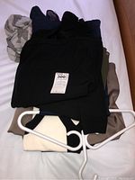 Folded pile of women's clothing including black, beige, white, and blue items with white hangers on top