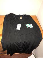 Long-sleeved black dress with tags laid on wood surface