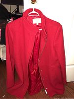 Red wool blend coat hanging on a hanger with open front showing red satin-like lining.