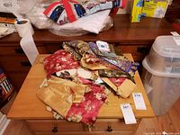 Pile of traditional style decorative linens including red and gold fabric with tassels and other folded fabrics.