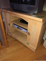 Front view of the veneered media cabinet showing two paneled side doors with ring pulls, two open shelves, and curved edge top surface with a TV on top.