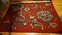 Full view of the Pier One wool area rug with floral design and red background on wood floor.