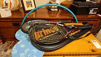 Two Prince tennis racquets with black holders, two floral patterned racquets, and blue hula hoop on wooden surface