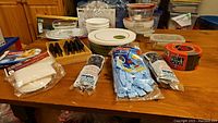 Photo showing various Corelle ceramic plates and bowls along with Gibson steak cutters, Vileda cleaning products, tape, and a Starfrit salad spinner on a wood table.