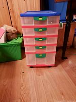 Front view of the Keter plastic storage cabinet showing five translucent drawers with red and green trim and handles, placed on wheels.