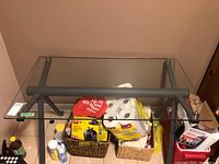 Full view of the rectangular table with transparent tempered glass top on a dark gray metal tubular frame base, surrounded by miscellaneous household items.