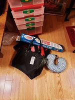 Overhead view of shoulder bag, travel pillow, laundry holder box, and folded red outdoor blanket on wooden floor