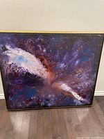 Full view of the framed abstract painting leaning against wall