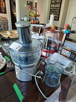 Breville juicer with large feeding chute, clear lid, and stainless steel body on table with juice container beside it. Untested condition.