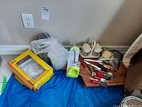 Wide view of the lot showing charcuterie board, various red-handled kitchen utensils, spiralizer, plastic bowls, and boxed plastic items on blue tarp.
