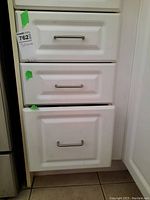 Three white kitchen drawers with silver handles closed, holding various kitchen utensils inside.