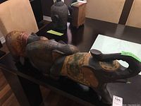 Three wooden elephant sculptures displayed on a table with visible painted patterns and intricate carvings, some wear evident.