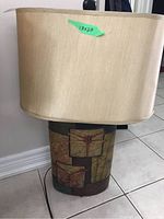 Full view of table lamp showing off beige fabric shade and decorative metal base with nature motifs.