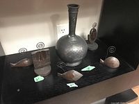 Photo of all items including the metal vase and four wood and metal figurines on a black shelf with size tags visible.