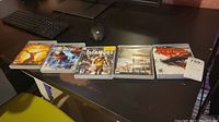 Five Playstation 3 game cases spread on table showing front cover artwork, includes God of War, Uncharted 2, Infamous, and two God of War games with one case missing disc