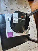 George Foreman toaster on top of Salton cooktop box on chair
