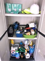 Overview of metal cabinet interior showing shelves with tools, chemical bottles, and safety gear including hard hats and yellow safety vests, as well as Campbell Hausfeld air compressor at the bottom shelf.