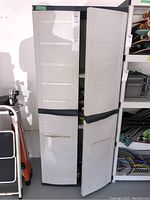 Front view of the plastic utility cabinet with both doors open, showing interior shelves and wear.