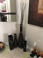 Four floor vases grouped together: two tall metal vases with decorative copper designs and two shorter black wooden vases.