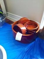 Large and small nested wooden salad bowls with salad utensils on blue tablecloth against wall with wood floor baseboard.