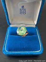Top view of ring showing round light green gemstone and four-prong setting in Birks box