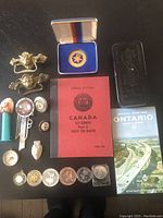 Photo showing an assortment of 18 collectibles, coins in a Canada Liberty 4 coin book, road map, pins, and door handles.