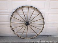 Front view of antique wooden wagon wheel showing full circular frame and multiple wooden spokes, one spoke missing.