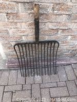 Front view of antique farm fork leaning against brick wall, showing wooden handle and metal fork head