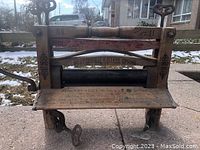 Front view of the antique wooden washing wringer showing the hand crank, black rollers, wooden frame with markings and floral stencil decoration.