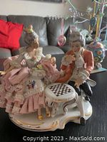 Front view of the Dresden porcelain figurine showing seated couple and baby with detailed clothing and checkerboard table.