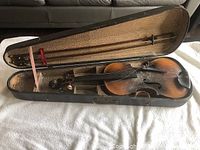 Violin inside old wooden case with two bows, showing overall lot contents and condition.