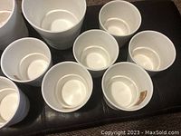 Top-down view of nine smaller and three larger white IKEA plastic flower pots arranged on surface.