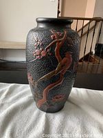 Front angle of black textured vase decorated with bird and flowering tree branch in raised relief.