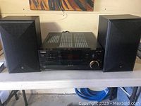 Front view of Pioneer Elite VSX-29TX receiver with two black Pioneer speakers on either side located on a white table.