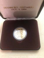 Commemorative coin in red velvet-lined display case with satin lid stating Sudbury, Ontario date