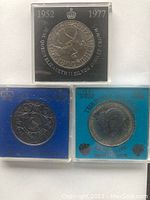 Front sides of three British commemorative coins in separate plastic cases, showing designs and inscriptions related to Queen Elizabeth II's Silver Jubilee and Royal Wedding.